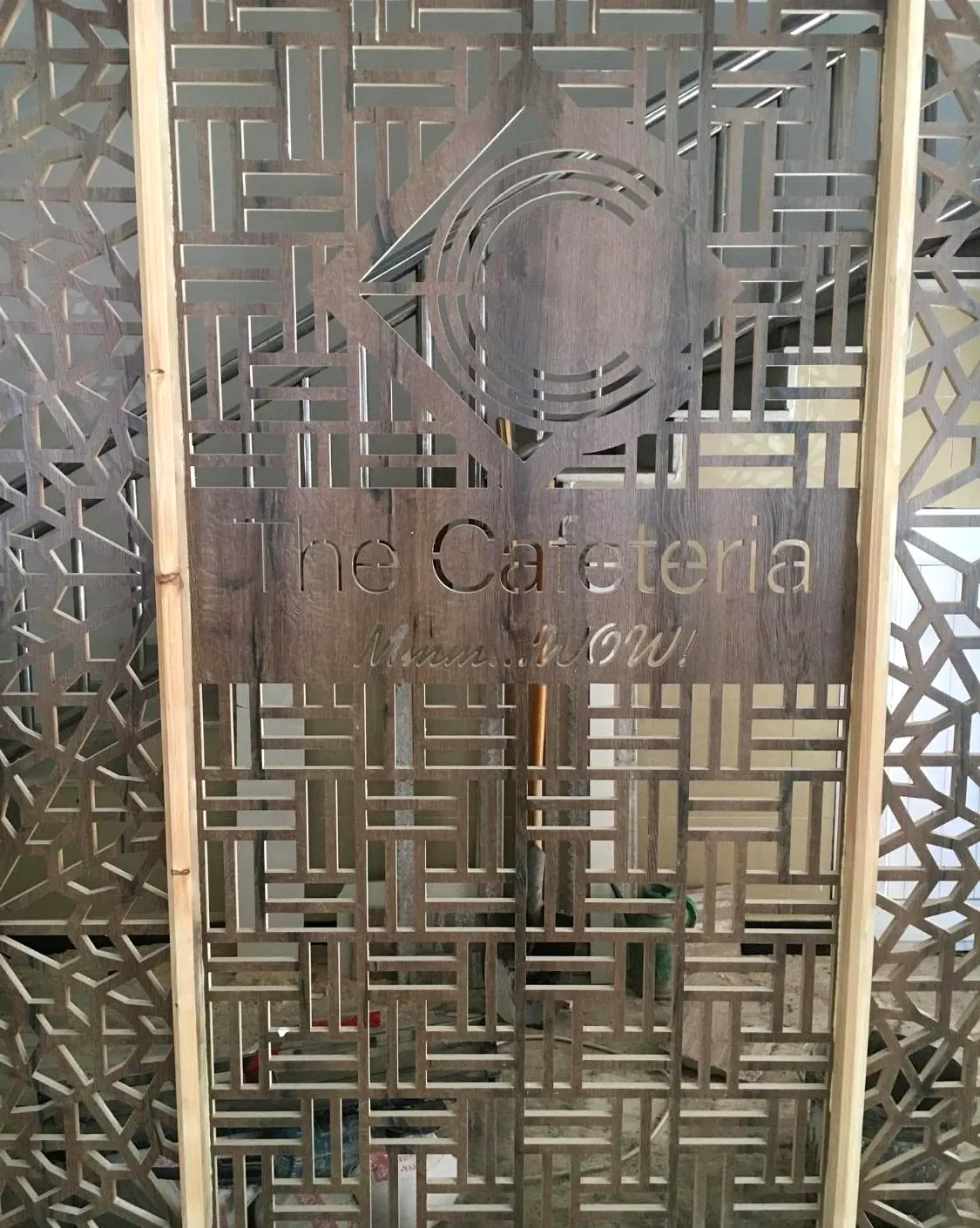 Laser-cut timber screen with a geometric lattice, The Cafeteria logo and the line Mmm WOW cut through it.