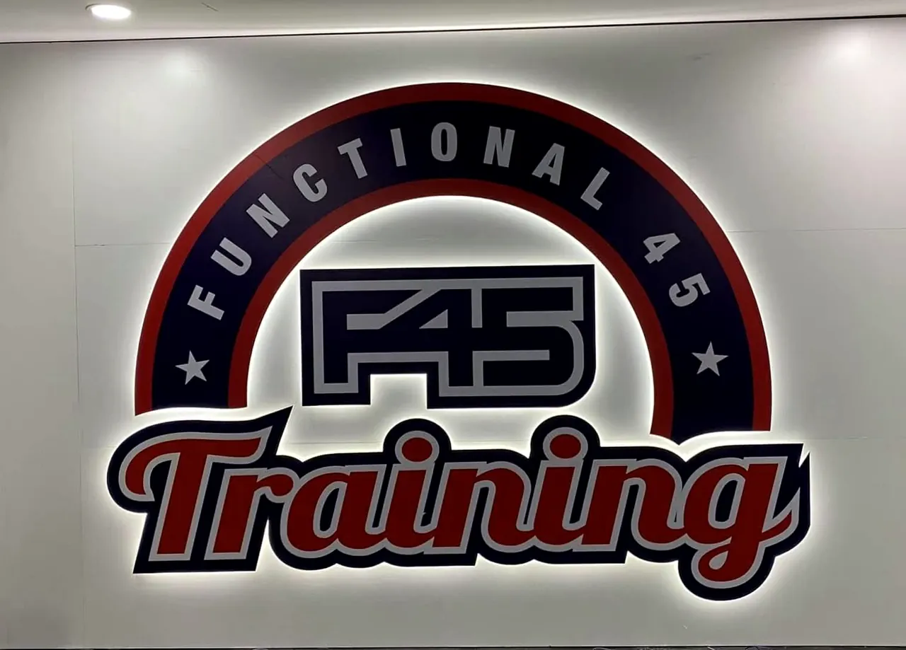Large F45 Training logo sign on a white gym wall, lit from behind so a white halo glows around the letters.