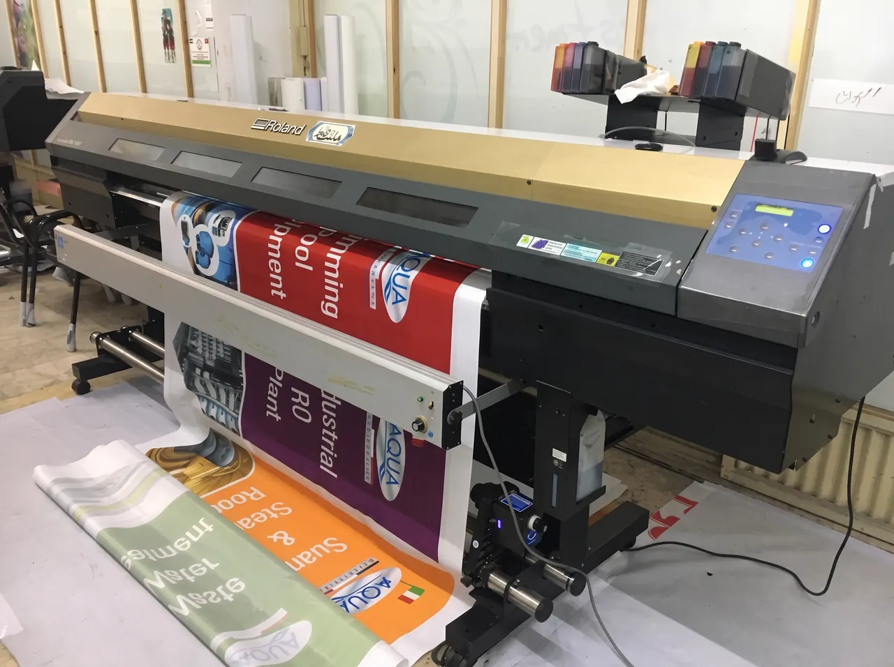 A Roland wide-format eco-solvent printer in the Wafa Sign workshop printing a run of colourful banners.